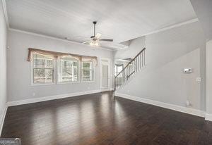 unfurnished living room featuring crown molding, baseboards, stairway, wood finished floors, and a ceiling fan