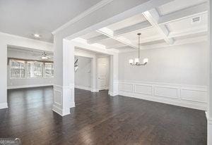interior space featuring beam ceiling, ornamental molding, coffered ceiling, a decorative wall, and a chandelier
