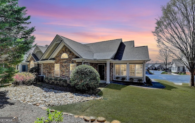 view of front of house featuring a front yard, stone siding, and a shingled roof