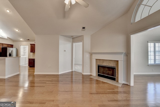 unfurnished living room featuring vaulted ceiling, a ceiling fan, light wood-type flooring, and a tile fireplace