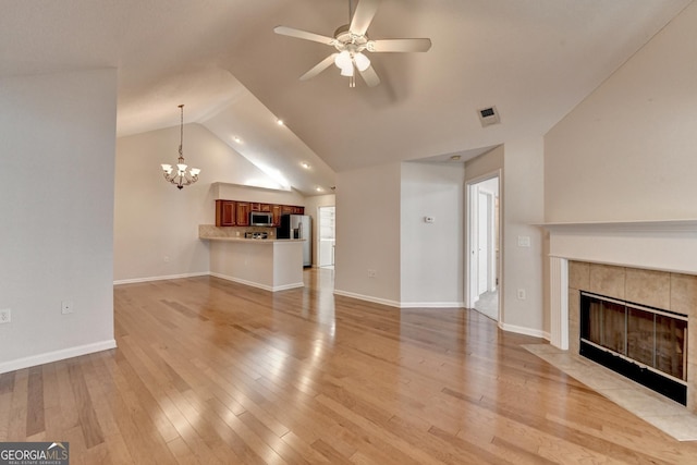 unfurnished living room featuring visible vents, light wood-style flooring, a fireplace, vaulted ceiling, and ceiling fan with notable chandelier