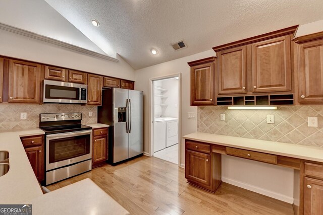 kitchen with light wood finished floors, washing machine and dryer, light countertops, vaulted ceiling, and stainless steel appliances