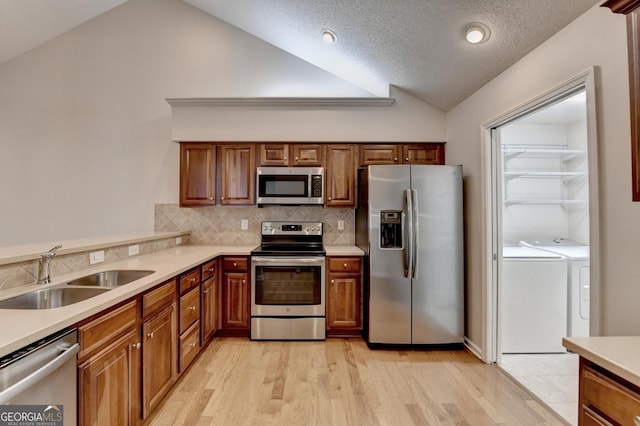 kitchen featuring washer and dryer, a sink, stainless steel appliances, light countertops, and vaulted ceiling