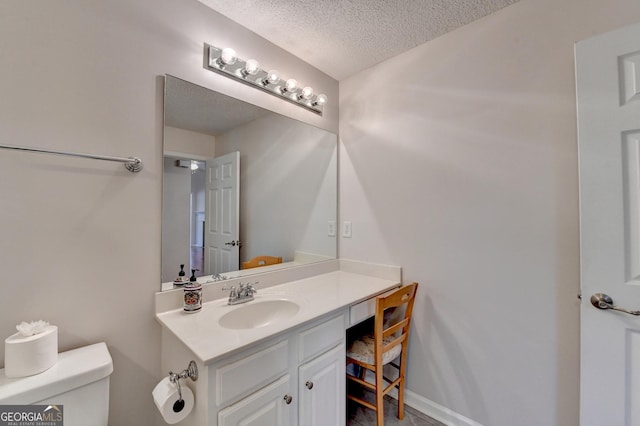bathroom featuring baseboards, toilet, vanity, and a textured ceiling