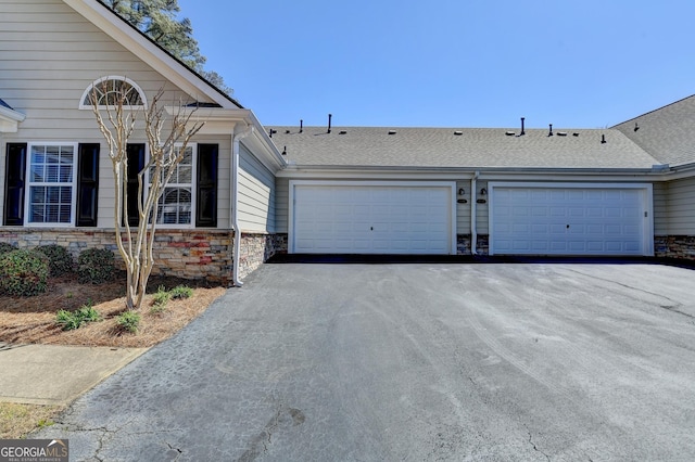 view of front facade with aphalt driveway, stone siding, and roof with shingles