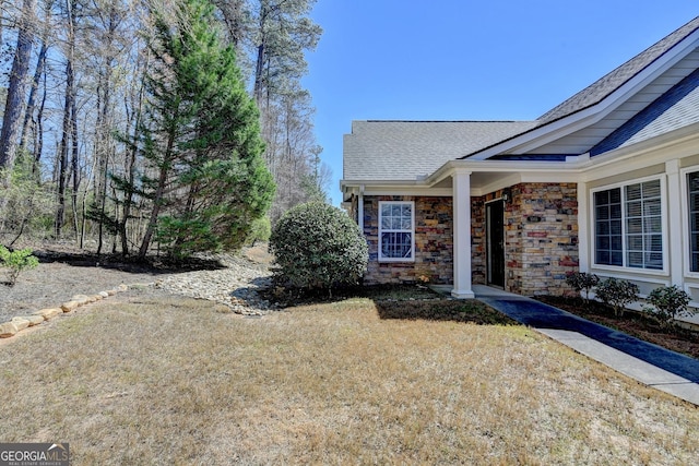 entrance to property with stone siding, a lawn, and roof with shingles