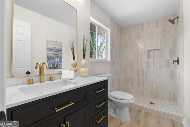 bathroom with tiled shower, toilet, wood finished floors, and vanity