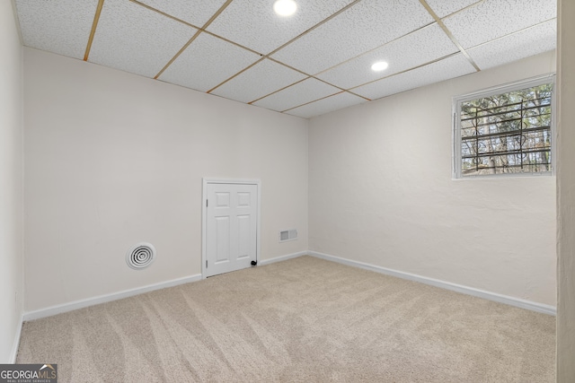 carpeted spare room featuring visible vents, a paneled ceiling, and baseboards
