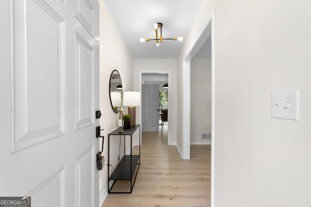 entrance foyer with light wood-style flooring, a notable chandelier, baseboards, and visible vents