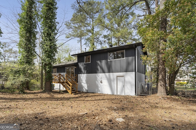rear view of house featuring board and batten siding, stairs, and fence