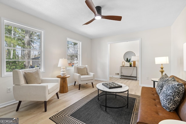 living area featuring baseboards, light wood-type flooring, and ceiling fan