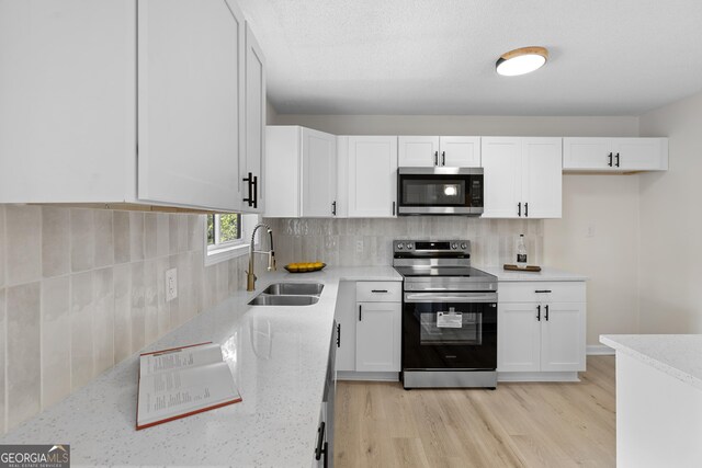kitchen featuring a sink, white cabinets, appliances with stainless steel finishes, tasteful backsplash, and light wood-type flooring