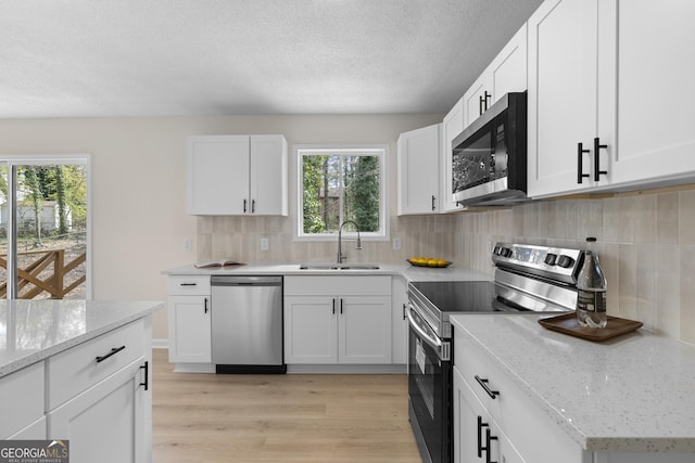 kitchen featuring light wood finished floors, decorative backsplash, appliances with stainless steel finishes, white cabinets, and a sink