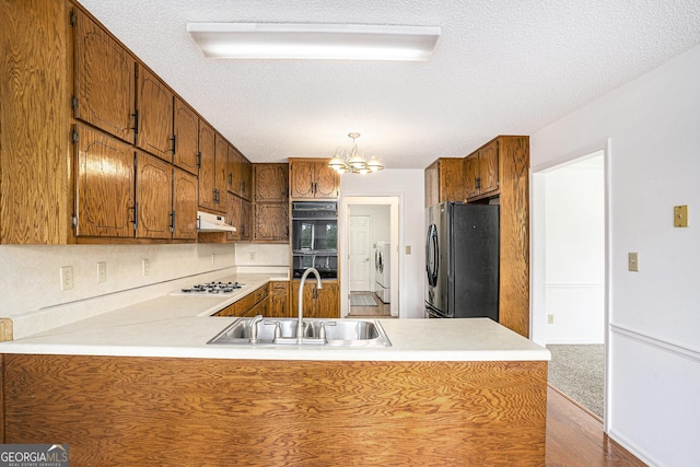 kitchen featuring a peninsula, black appliances, a sink, independent washer and dryer, and a notable chandelier