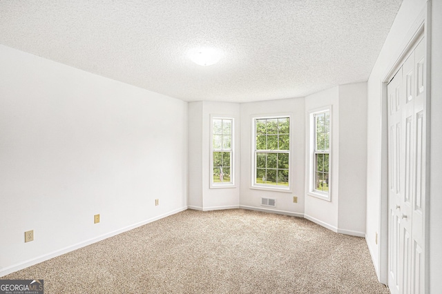 unfurnished bedroom with baseboards, carpet, a textured ceiling, and visible vents