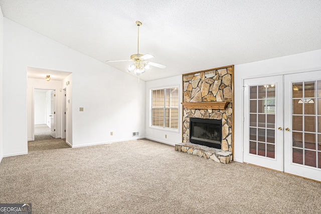 unfurnished living room with carpet flooring, a stone fireplace, french doors, baseboards, and lofted ceiling