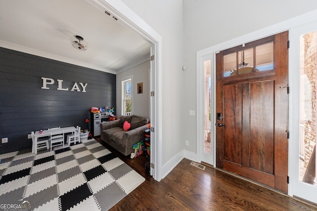 foyer entrance with baseboards, crown molding, wood walls, visible vents, and wood finished floors