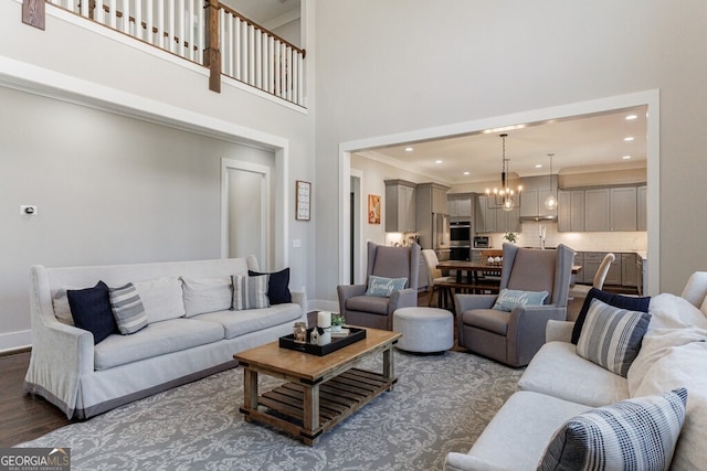 living area featuring a notable chandelier, baseboards, ornamental molding, dark wood-style floors, and a high ceiling