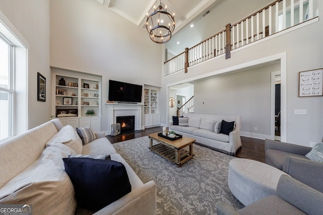 living area with an inviting chandelier, a warm lit fireplace, stairway, wood finished floors, and a towering ceiling