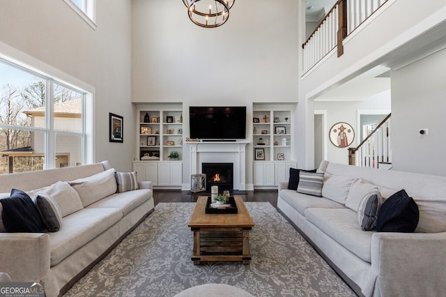 living room with a notable chandelier, wood finished floors, stairs, a towering ceiling, and a lit fireplace