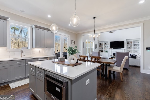 kitchen featuring crown molding, dark wood finished floors, a kitchen island, a sink, and gray cabinetry