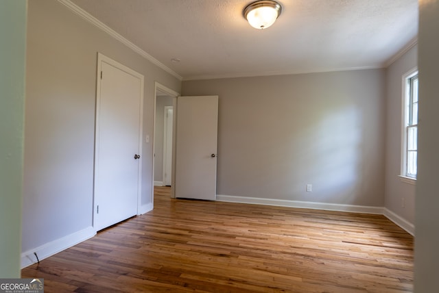 empty room with wood finished floors, ornamental molding, and baseboards