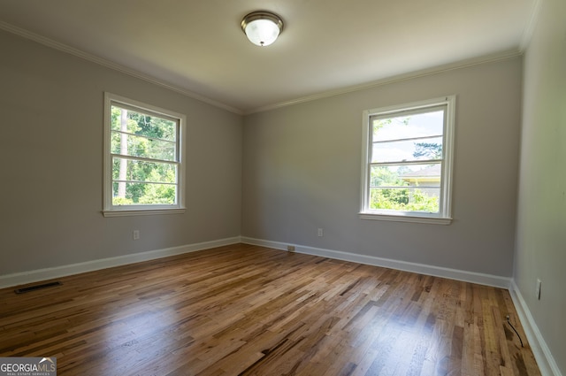 empty room with plenty of natural light, wood finished floors, ornamental molding, and baseboards