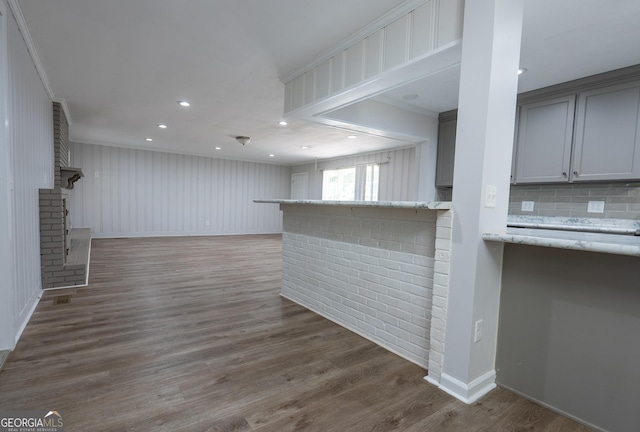 unfurnished living room with ornamental molding, wood finished floors, a brick fireplace, baseboards, and recessed lighting