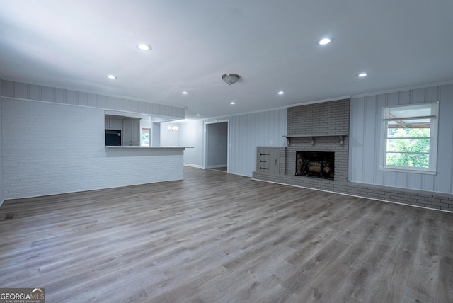 unfurnished living room with crown molding, brick wall, a brick fireplace, wood finished floors, and recessed lighting