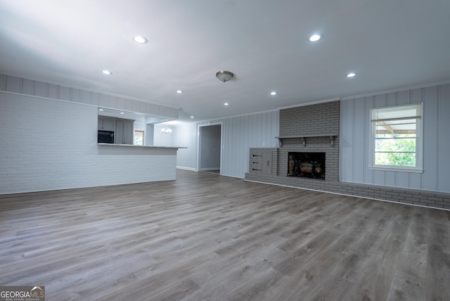 unfurnished living room featuring ornamental molding, wood finished floors, a fireplace, brick wall, and recessed lighting