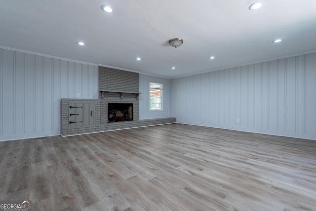 unfurnished living room featuring crown molding, wood finished floors, a brick fireplace, recessed lighting, and a decorative wall