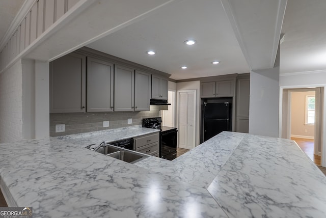 kitchen featuring black appliances, under cabinet range hood, a sink, backsplash, and ornamental molding