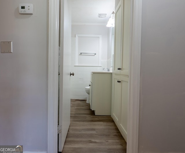 hallway featuring crown molding, wood finished floors, and tile walls
