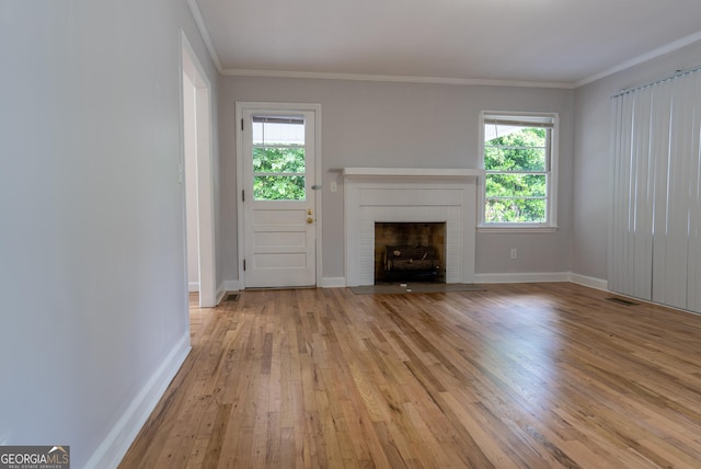 unfurnished living room with light wood-type flooring, plenty of natural light, a brick fireplace, baseboards, and crown molding
