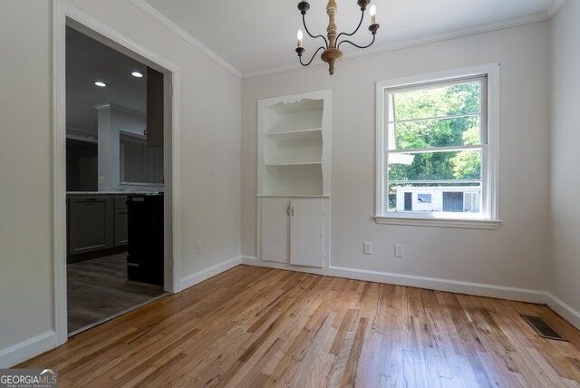 unfurnished dining area with a chandelier, crown molding, light wood-style flooring, and baseboards