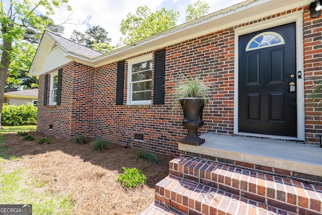 view of exterior entry featuring brick siding and crawl space