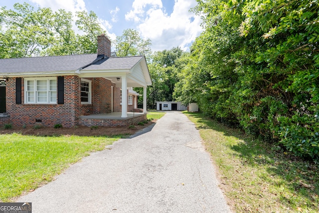 view of side of property featuring brick siding, a chimney, driveway, an outbuilding, and roof with shingles