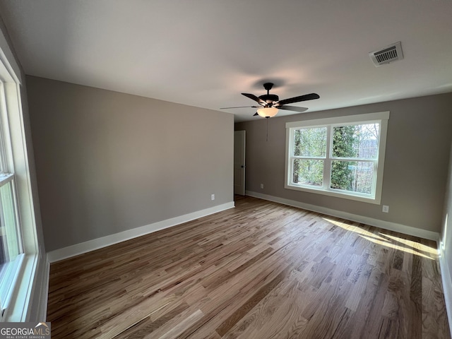 unfurnished room with baseboards, wood finished floors, visible vents, and ceiling fan