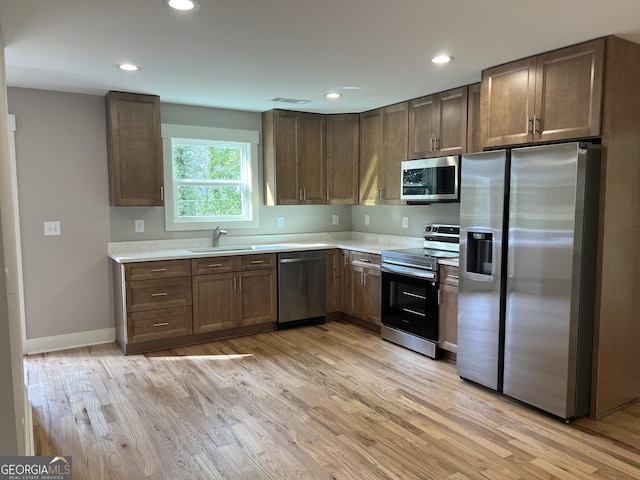 kitchen with light wood-type flooring, stainless steel appliances, light countertops, and a sink