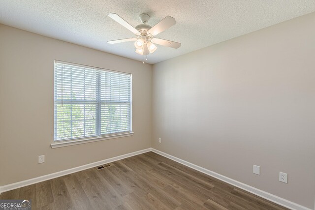 spare room with a textured ceiling, ceiling fan, dark wood finished floors, baseboards, and visible vents