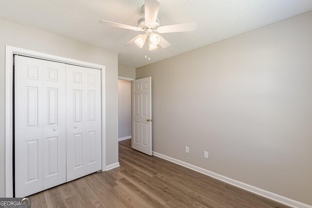 unfurnished bedroom with a textured ceiling, baseboards, wood finished floors, a closet, and ceiling fan