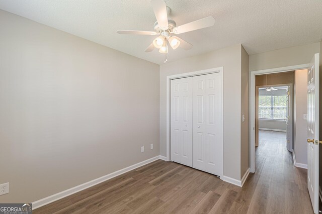 unfurnished bedroom with wood finished floors, a closet, a ceiling fan, and baseboards
