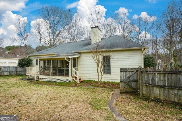 rear view of property featuring a gate, a chimney, fence, a lawn, and a sunroom