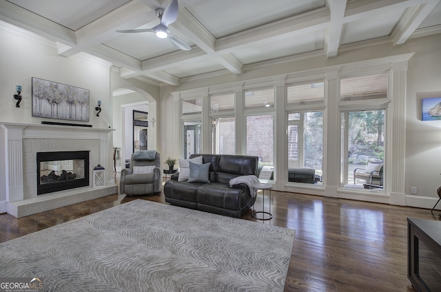 living area with a brick fireplace, arched walkways, beamed ceiling, a ceiling fan, and wood finished floors