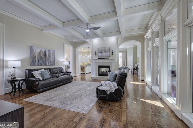 living area featuring arched walkways, ceiling fan, wood finished floors, and beamed ceiling