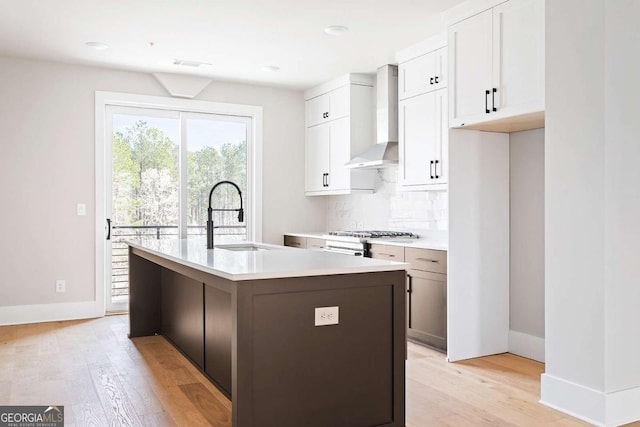 kitchen featuring wall chimney exhaust hood, a sink, light wood finished floors, tasteful backsplash, and light countertops