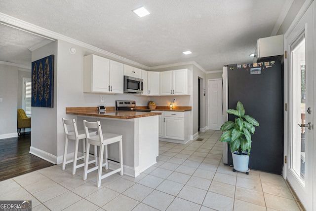 1875 Ebenezer Rd SW, Conyers, GA 30094 - kitchen featuring stainless steel appliances, wood counters, a textured ceiling, white cabinetry, and light tile patterned floors