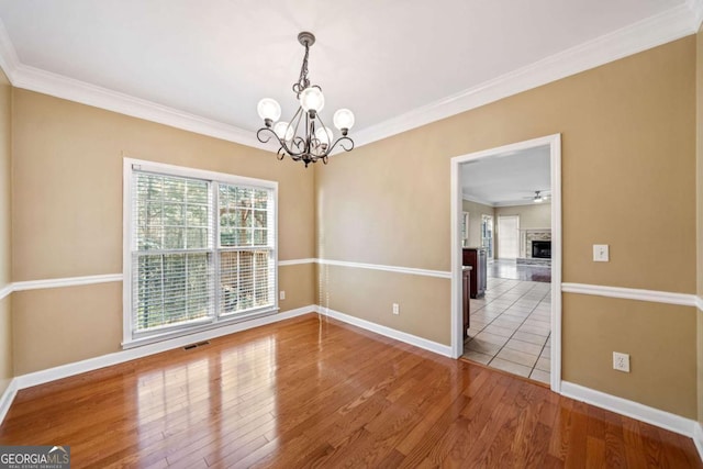 empty room with a notable chandelier, crown molding, visible vents, and wood finished floors