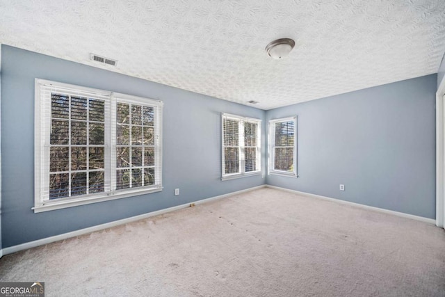 empty room featuring carpet, baseboards, visible vents, and a textured ceiling