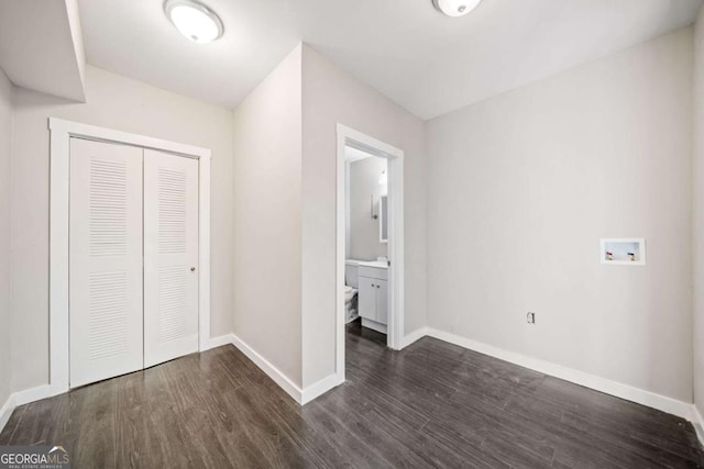 unfurnished bedroom with a closet, ensuite bath, dark wood-type flooring, and baseboards